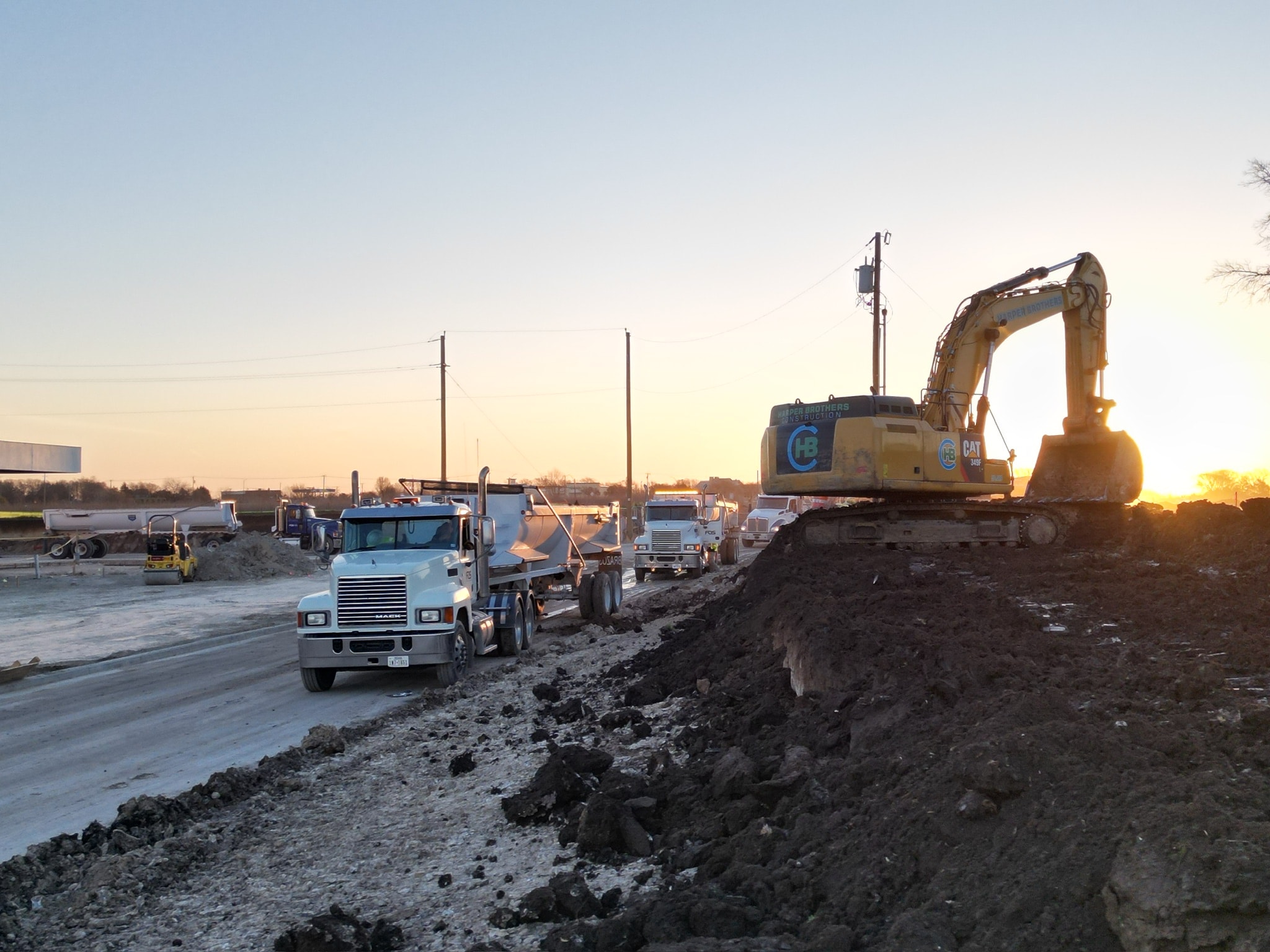 FOS Logistics trucks lined up at a road construction project at sunset
